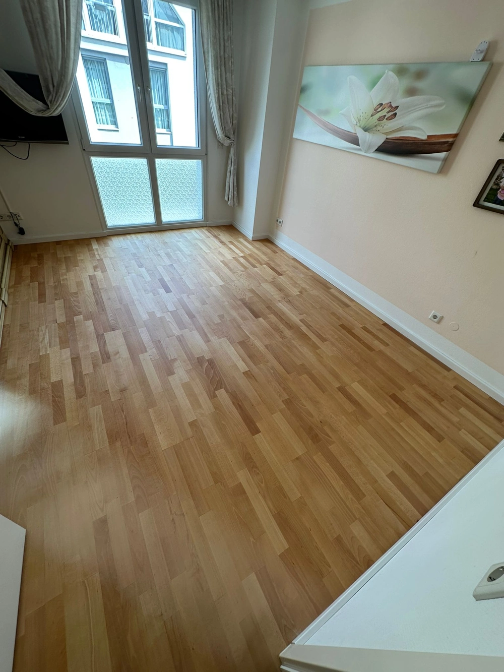 Leerer Raum mit neu verlegtem Parkettboden, großer Fensterfront und Blütenbild an der Wand – Parkett verlegen