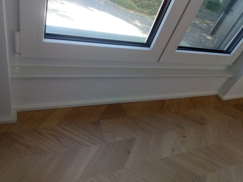 Große Fensterfront mit weißer Fensterbank und neu verlegtem Fischgrätparkett im Rahmen von Parkett verlegen