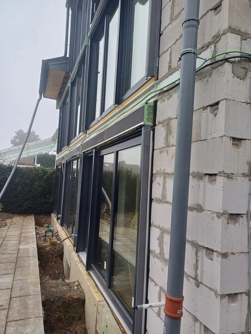 Fassadenbau: Porenbetonwand mit eingebauten Fensterelementen, Regenfallrohr und Geländevorbereitung