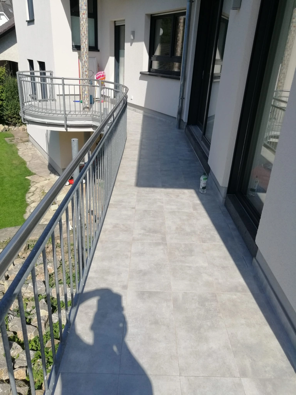 Moderner Balkonflur mit hellgrauen Bodenfliesen und Stahlgeländer an weißer Fassade, Balkonbau