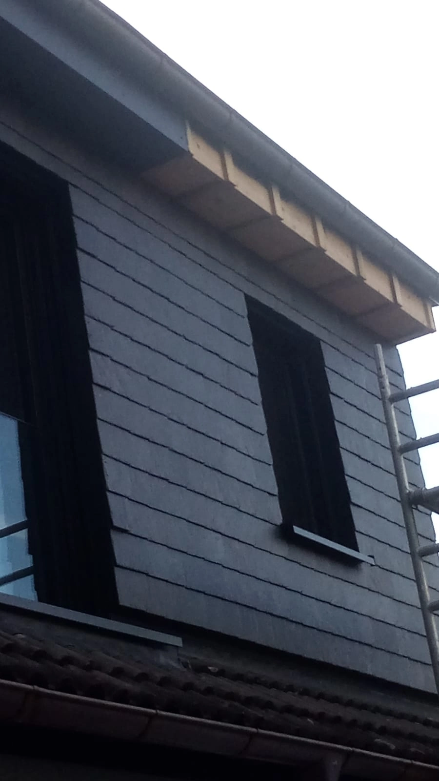 Graue Schieferfassade mit neuem Dachüberstand und schwarzen Fensterläden, Fassadenbau