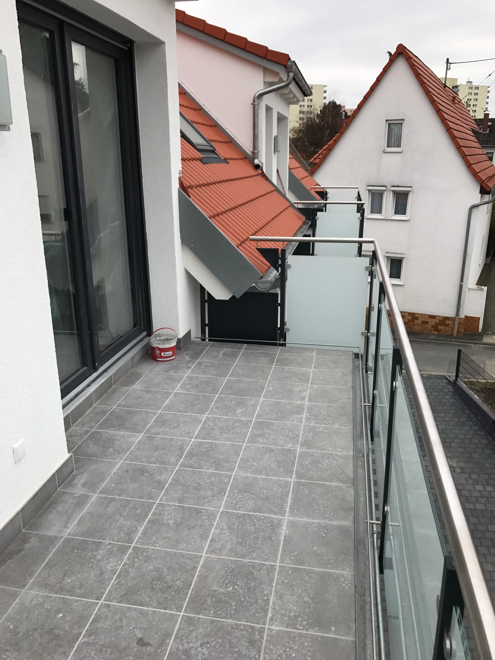 Moderner Balkon mit grauen Bodenfliesen und Glasgeländer als Beispiel für Balkon bauen