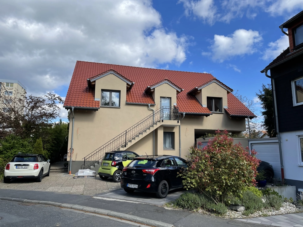 Fassadenbau an zweistöckigem Wohnhaus mit Putzfassade und Außentreppe, davor geparkte Autos
