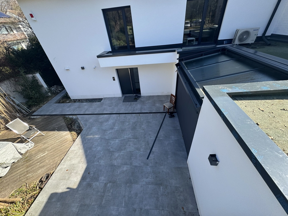 Moderne gepflasterte Terrasse mit großformatigen grauen Bodenfliesen vor Neubau-Fassade (Terrassenbau)
