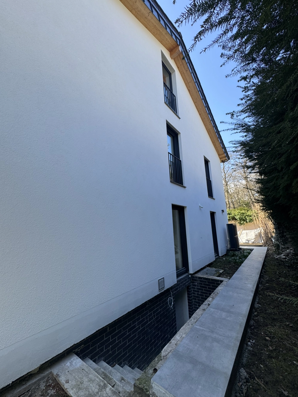 Seitlicher Blick auf neu verputzte weiße Fassade mit Kellerzugang und Betongehweg – Fassadenbau