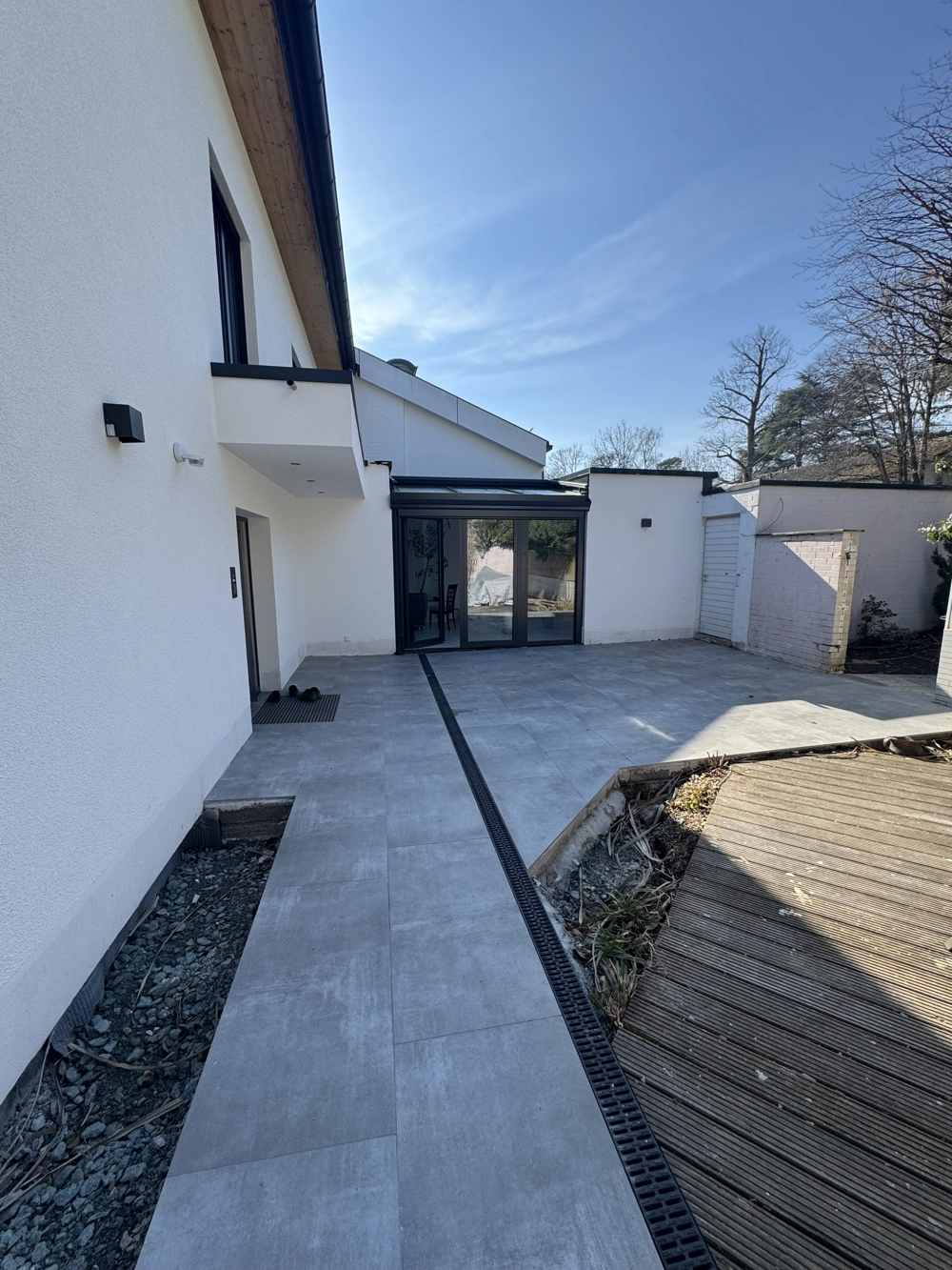 Terrassenbau: Neu errichtete Terrasse mit großformatigen grauen Fliesen und moderner Glasfront an weißem Einfamilienhaus