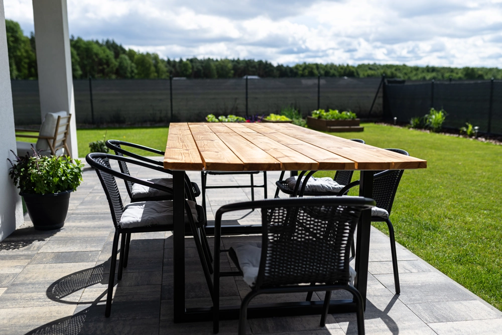 Terrassenbau mit Holztisch und schwarzen Gartstühlen auf gefliester Terrasse im Garten