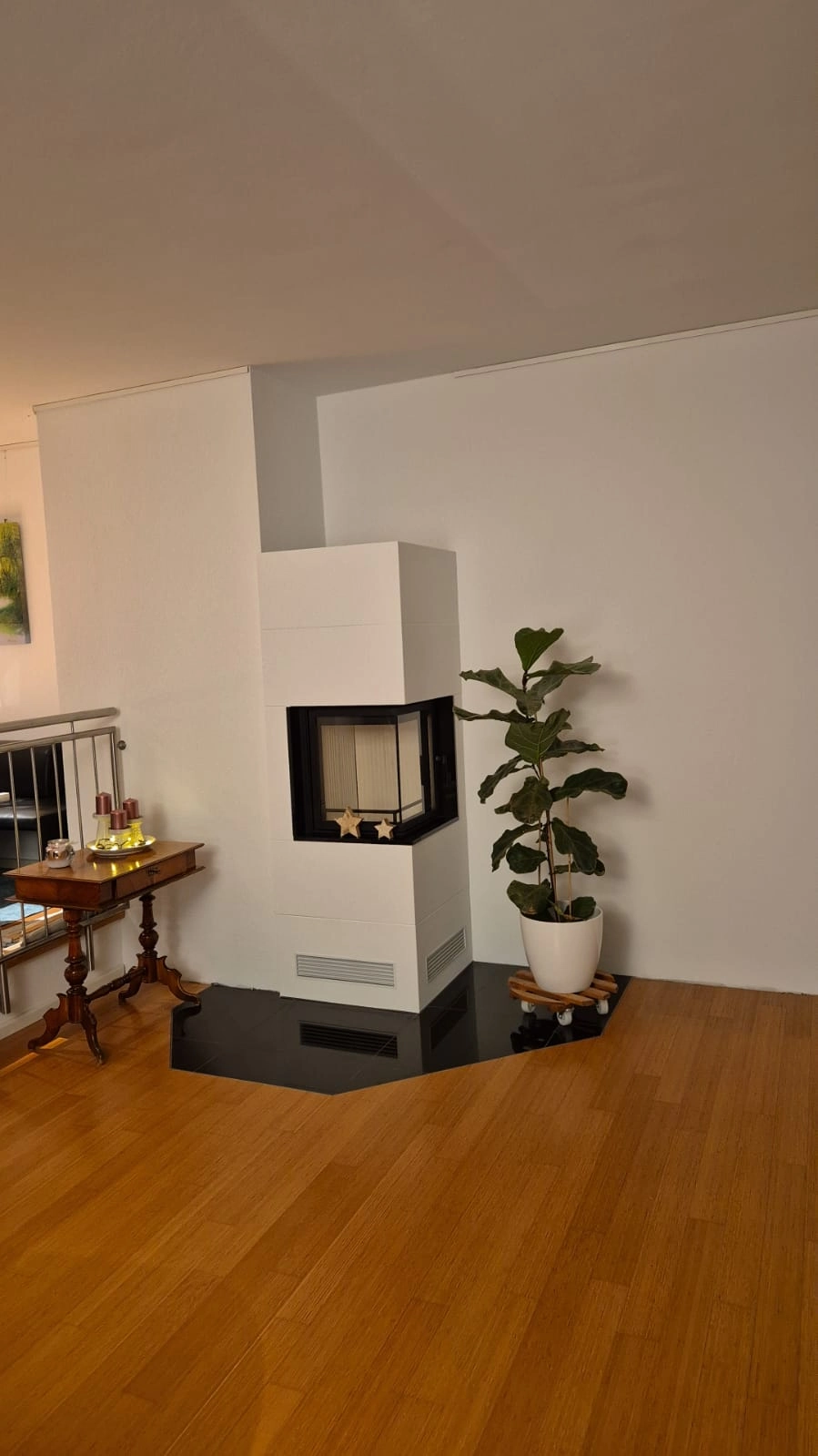 Moderner weißer Eckkamin im hellen Wohnraum mit Parkettboden und Zimmerpflanze als Wohnraumgestaltung
