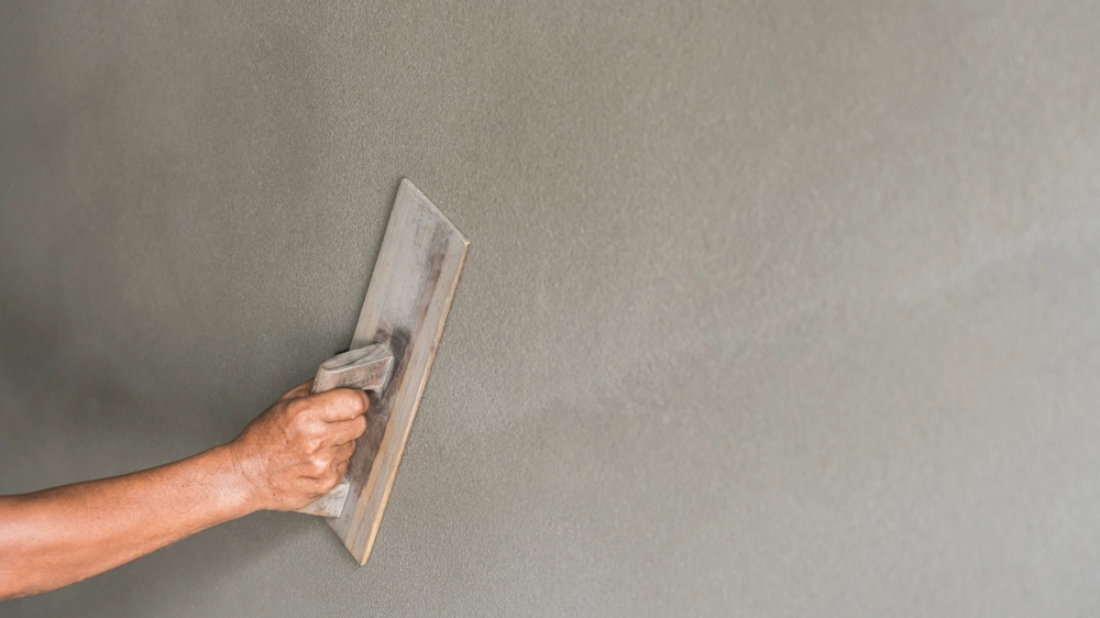 Nahaufnahme einer Hand, die mit Glättkelle Putzarbeiten an einer glatten Innenwand ausführt