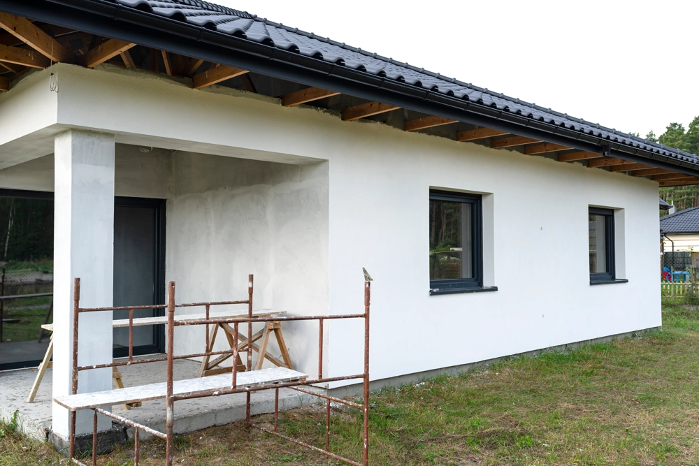 Hausfassade mit Gerüst und frisch aufgetragenem Putz – Putzarbeiten am Einfamilienhaus