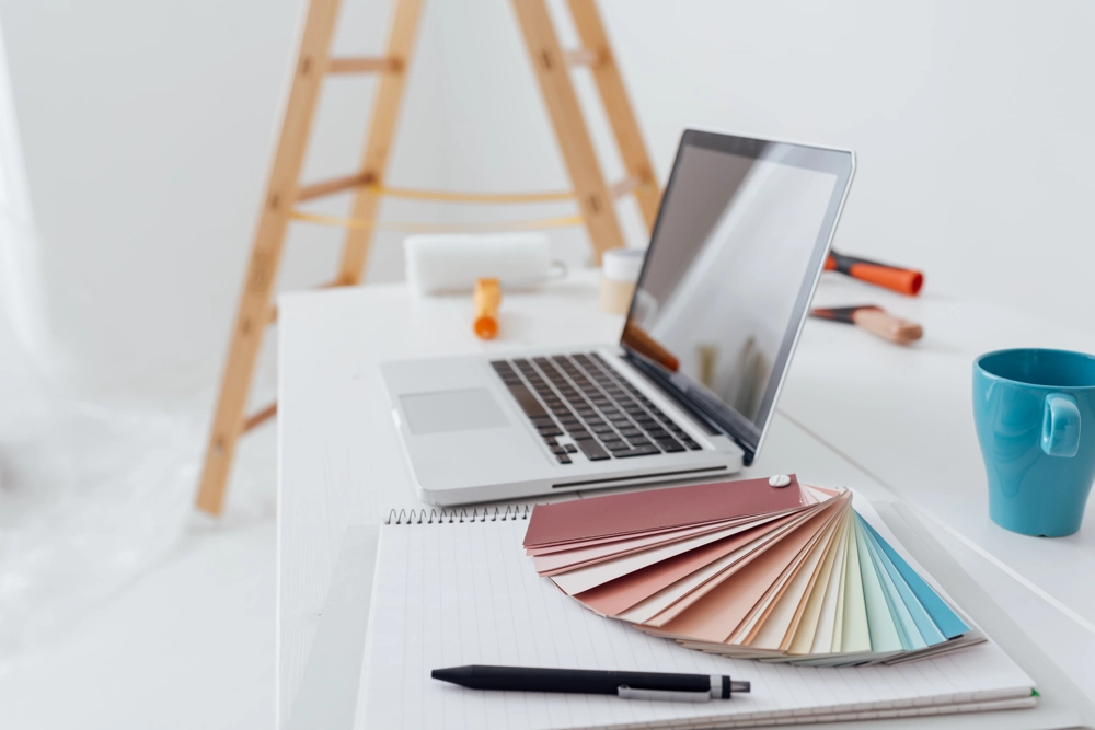 Arbeitsplatz mit Laptop, Farbfächer, Notizblock und Stift für Innenraumgestaltung und Farbkonzepte