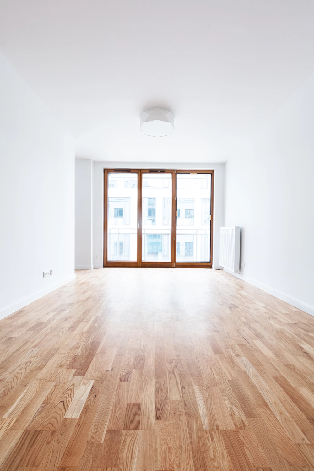 Leerer, heller Wohnraum mit frisch verlegtem Parkettboden und bodentiefen Fenstertüren