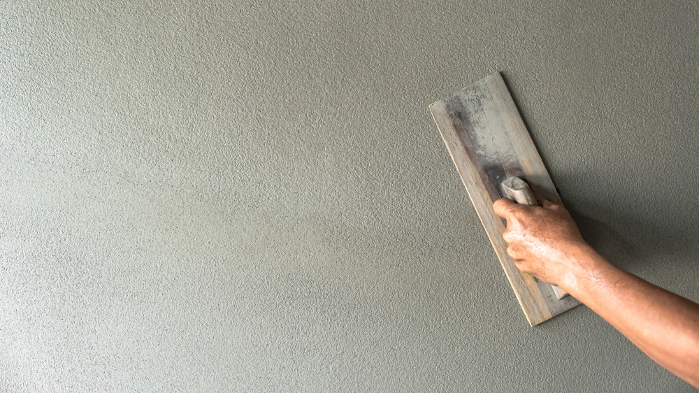 Hand mit Glättkelle bei Putzarbeiten an glatter Wandoberfläche