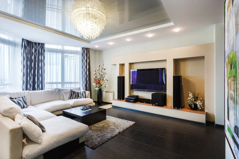 Modern ausgestattetes Wohnzimmer mit L-Sofa, TV-Wand, Hängedecke und Fliesenboden im Rahmen des Innenausbaus