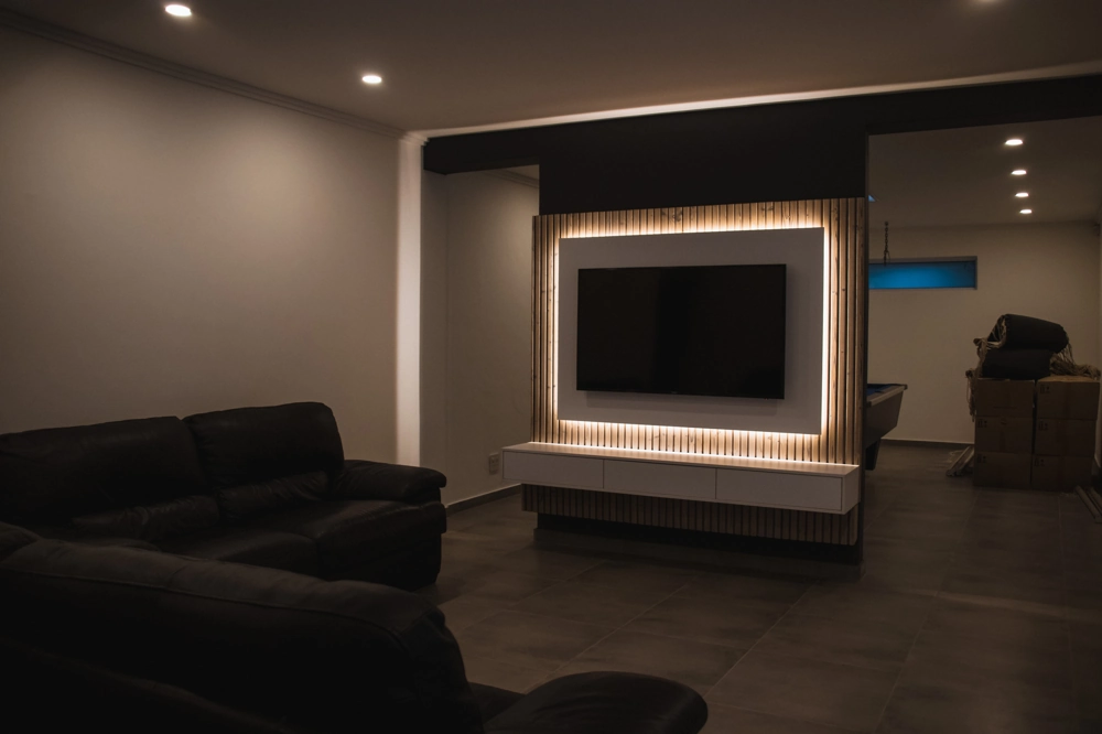 Moderne Kellereinrichtung mit LED-beleuchteter TV-Wand, Deckenspots und Ledersofas (Innenausbau)
