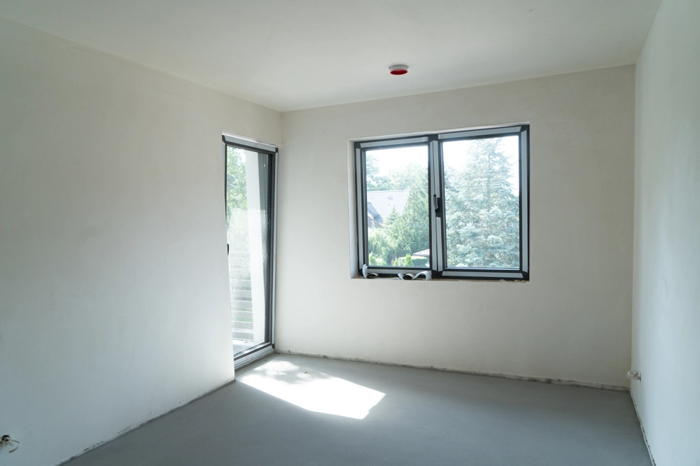 Leerer Wohnraum mit frisch verputzten Wänden, großen Fenstern und Zugang zu Terrasse – Putzarbeiten im Innenausbau