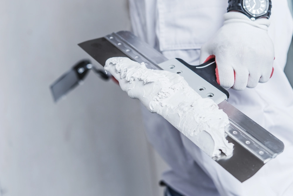 Nahaufnahme einer Hand mit Spachtel und frischer Spachtelmasse bei Spachtelarbeiten am Innenausbau