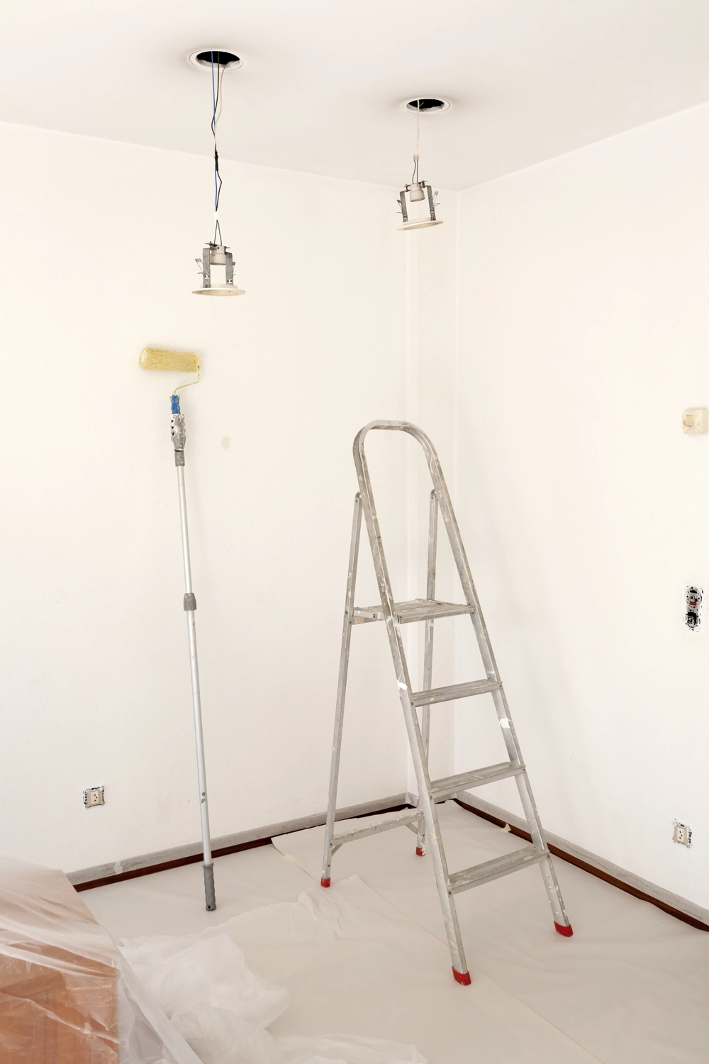Aluminiumleiter und Farbschaumroller mit Abdeckfolie in weiß gestrichenem Zimmer bei Malerarbeiten