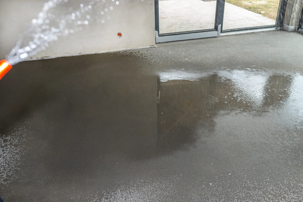 Frisch aufgebrachter Estrichboden im Innenraum, mit Wasser besprüht zur Aushärtung